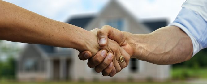 Real estate agent shaking hands with buyer in front of house