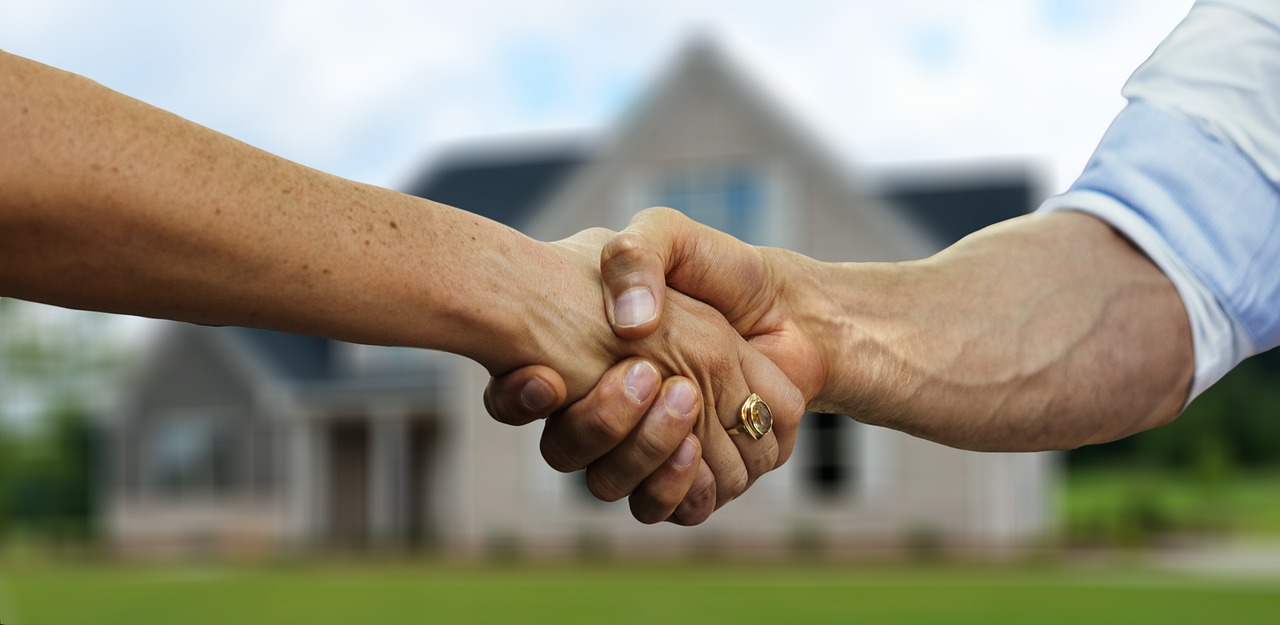 Real estate agent shaking hands with buyer in front of house